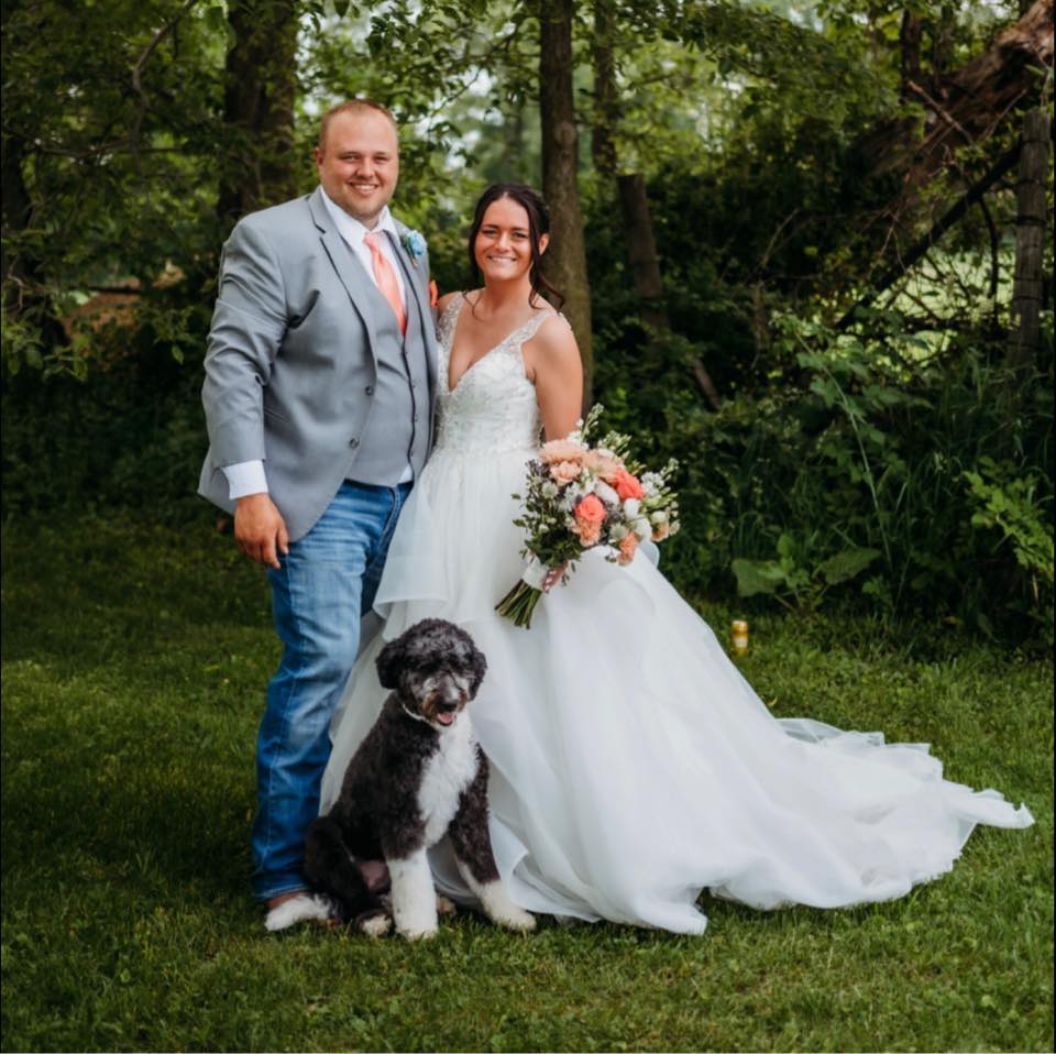 A bride and groom with their dog on a grassy area