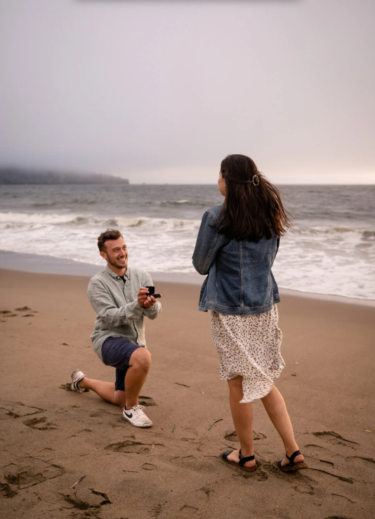 A woman in a wedding dress is standing in front of the sea on the rocks.